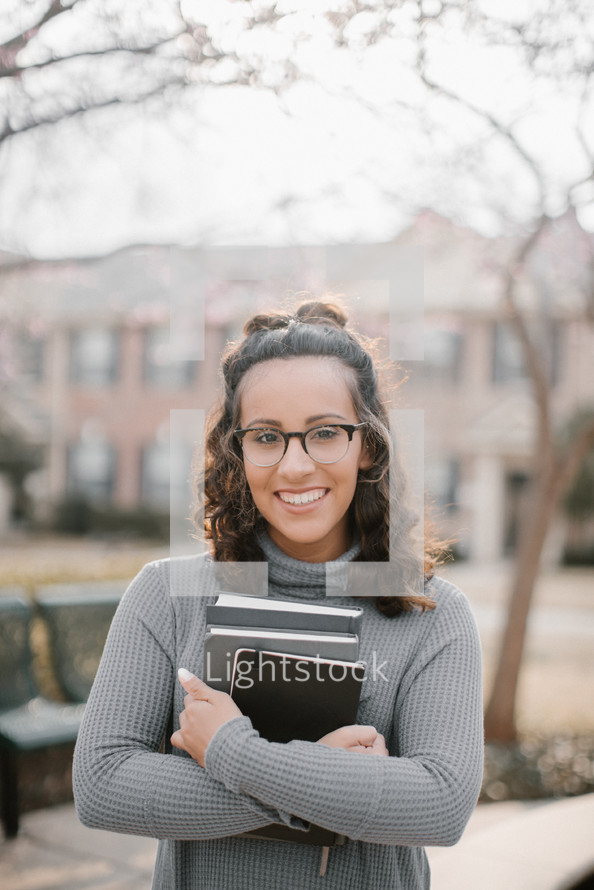 a young woman holding a stack of books on campus 
