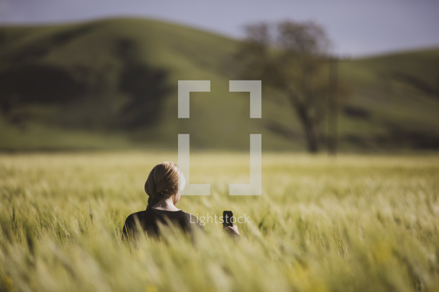 a woman holding a cellphone standing in a field of tall grasses 
