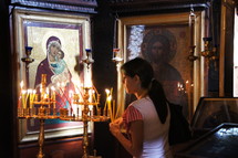 Lighting a votive or prayer candle before icons of Christ and Mary the mother of Christ 