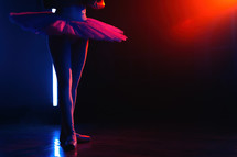 Ballet dancer's legs in pointe shoes on theater stage. Ballerina standing in 3 third position on neon colorful background. Beautiful woman's feet. Lady shows classic pas. Copy space.
