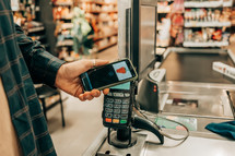 Customer buying food from cashier and paying at the till. Supermarket store. Man paying with contactless credit card in smartphone in grocery store