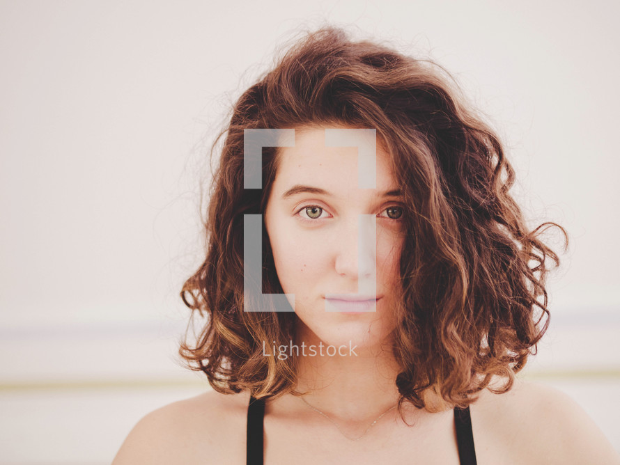 Portrait of young pretty yoga girl with short curly hair in sportwear. Calm and peace on her face. Slight smile.