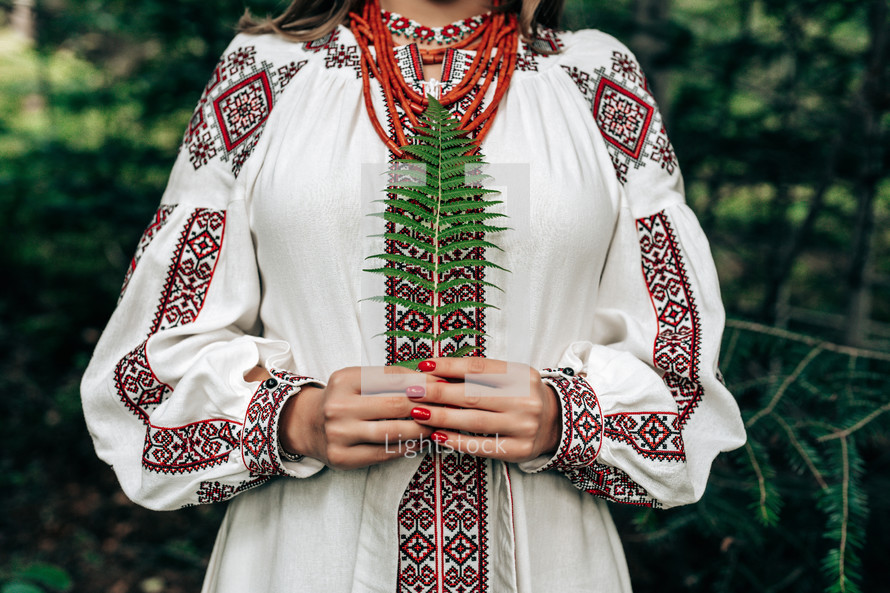 Authentic woman in traditional ukrainian costume with fern in forest. Lady in national dress - vyshyvanka, ancient coral beads. High quality photo