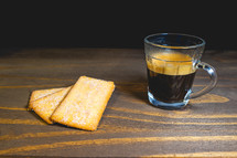 Glass cup of expresso with biscuits on a wooden table.