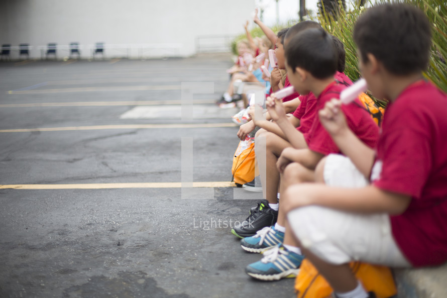 children eating popsicles sitting on the curb