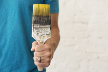 A married man holding a paint brush with yellow paint.