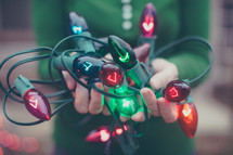 A woman holding a tangle of red and green Christmas lights.