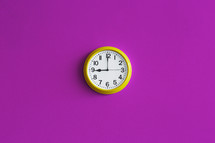 A yellow wall clock on a bright pink wall.