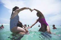 teen girl swimming in the ocean making a heart with their arms 