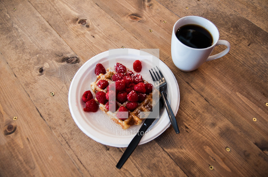 a waffle with raspberries and a coffee mug 