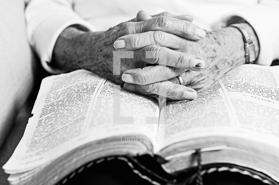 Elderly folded hands on the pages of an open Bible.