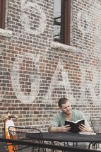 man reading a Bible sitting at an outdoor cafe