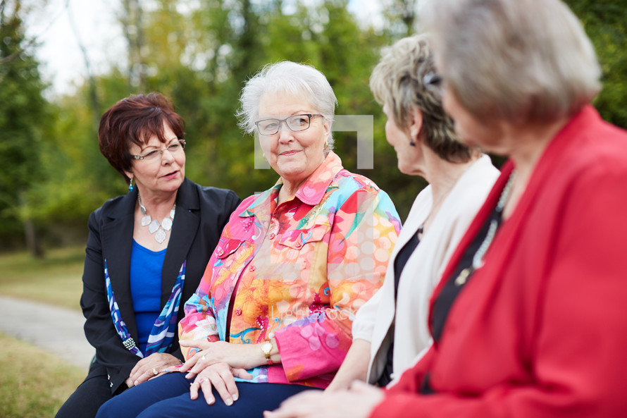elderly women talking sitting on a bench outdoors 