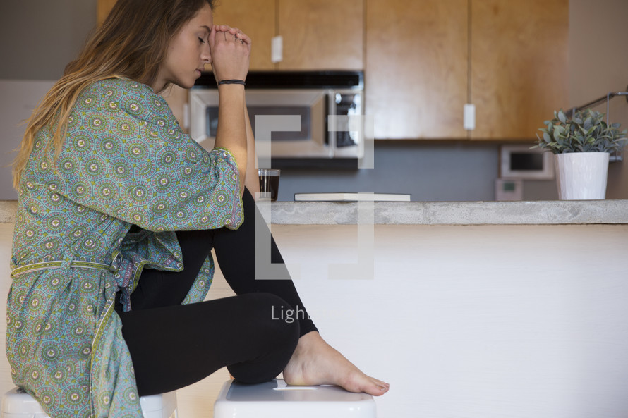 a woman in her pajamas praying in the kitchen