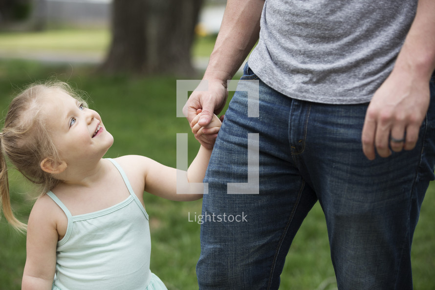 A smiling young girl holding her father's hand and looking up at him.