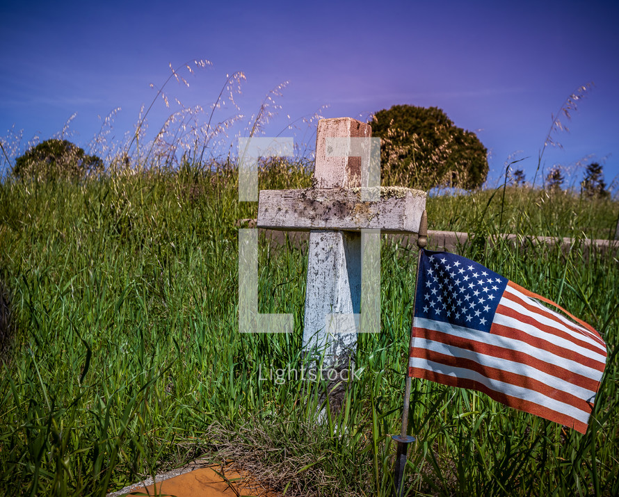American flag next to a cross grave marker in an old cemetery 