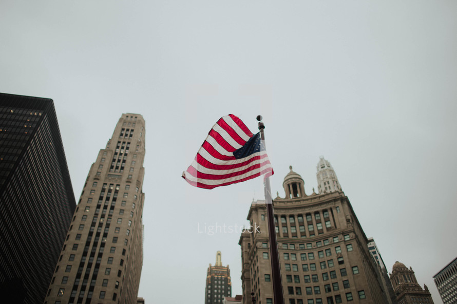 American flag on a flagpole and city buildings 