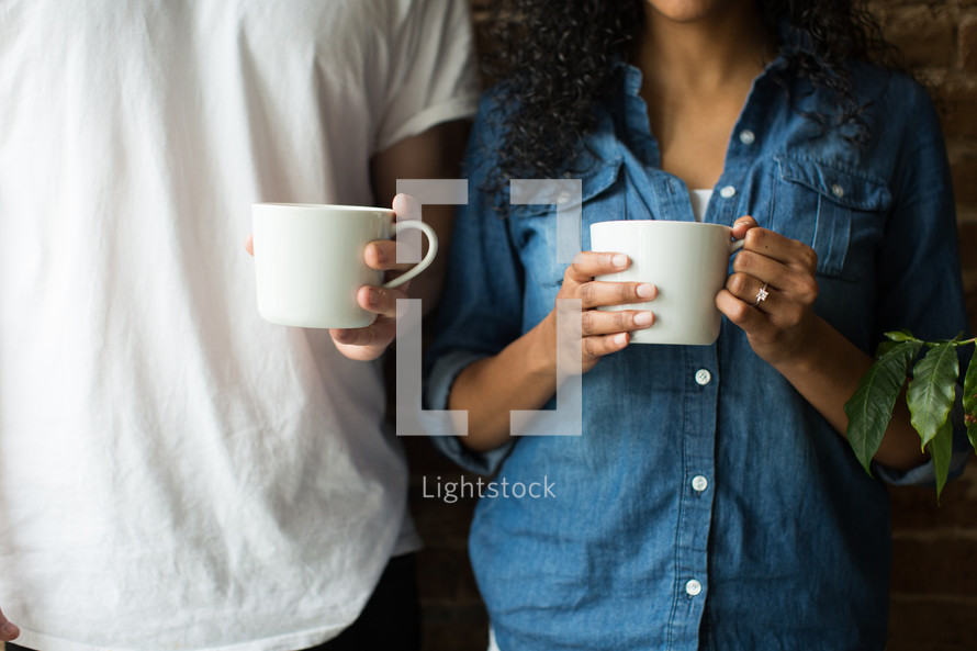 A man and woman standing and holding coffee cups.