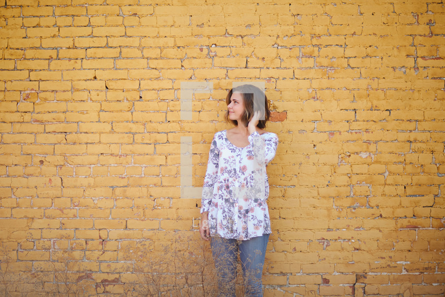 a woman standing in front of a yellow brick wall 