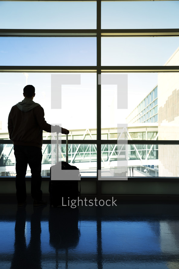 A man with luggage starring out an airport window 
