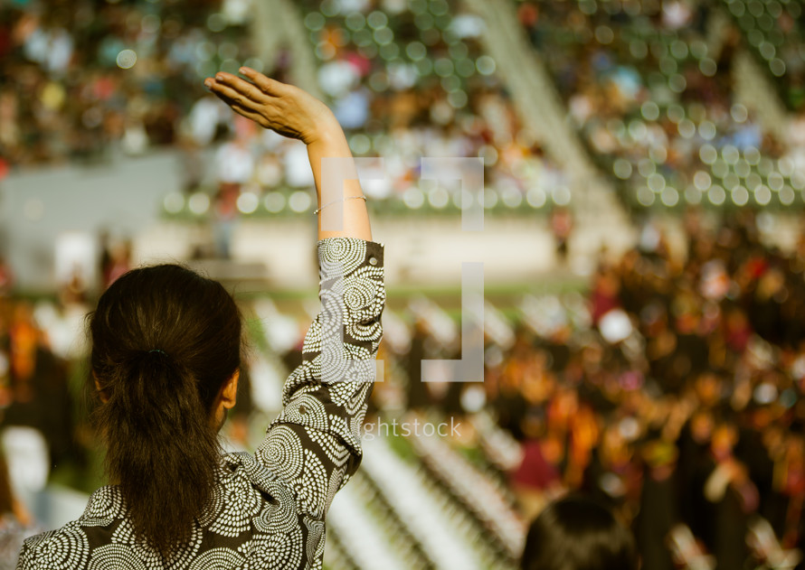 A woman in the audience with raised hand at a graduation ceremony.