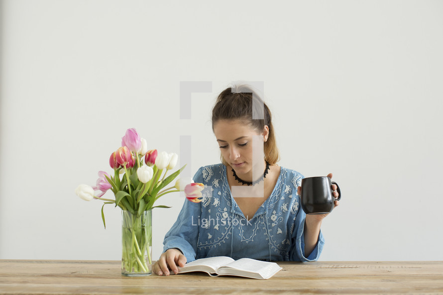 a woman sitting at a desk with a mug of coffee and a vase of tulips 