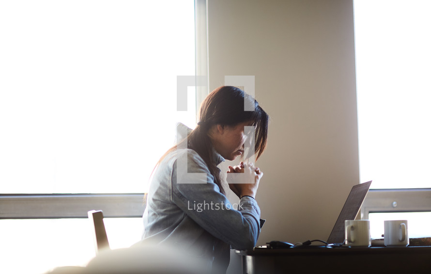 a woman praying in front of a laptop computer 