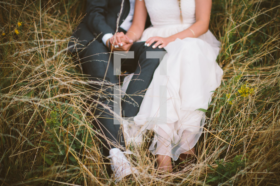 bride and groom sitting in a field 