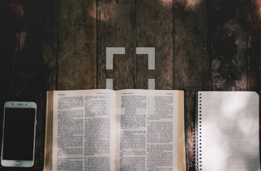 cellphone, open Bible, notebook, on a wood background 