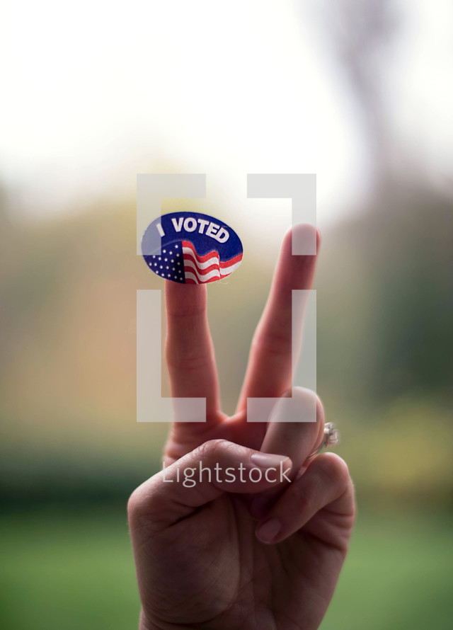 hand holding up a peace sign and a I voted sticker 
