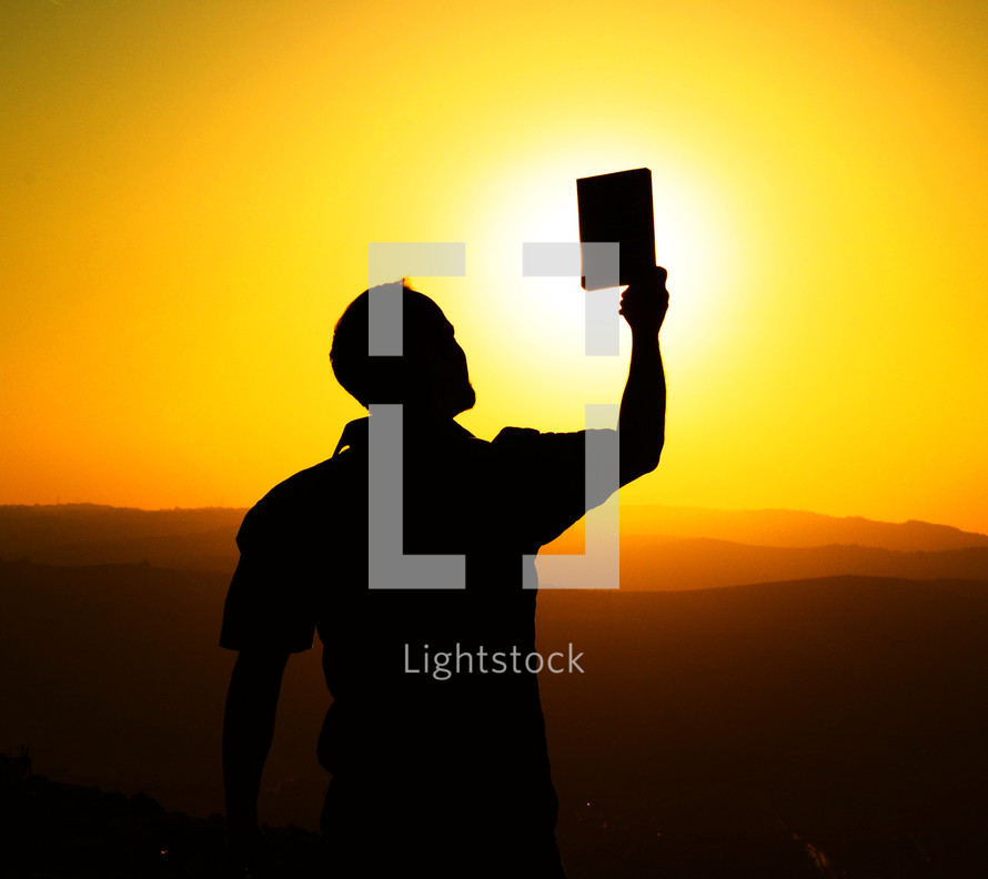 silhouette of a man holding up a Bible 