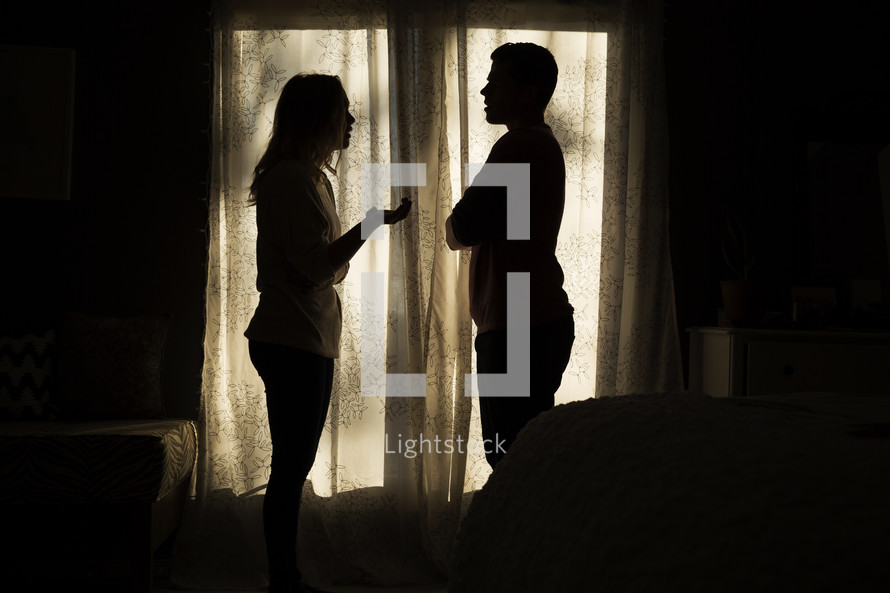silhouette of an arguing couple in front of a window. 