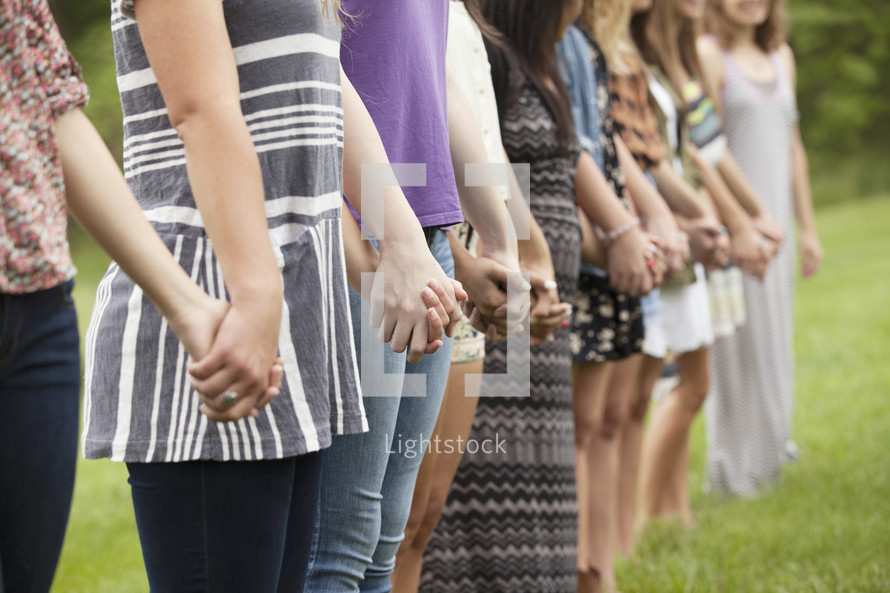 Line of women standing outside holding hands.
