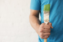 A man holds a paint brushes with green paint.