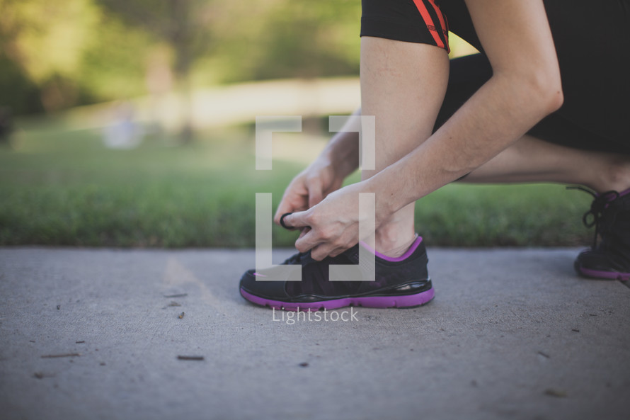 Runner tying shoes on a sidewalk.