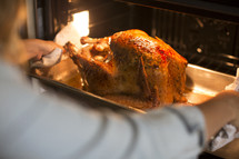 a woman pulling a turkey out of the oven.