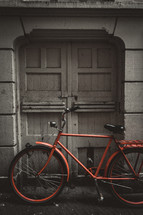 red bicycle parked in front of gray doors 