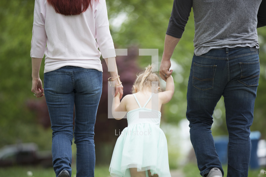 a mother, father, and toddler, daughter walking holding hands 