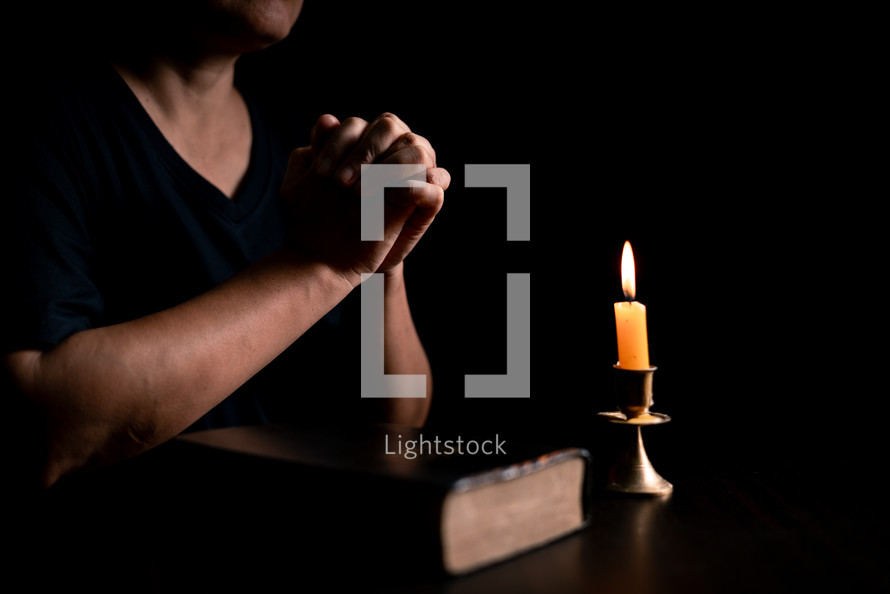 Bible and candlelight with praying hands