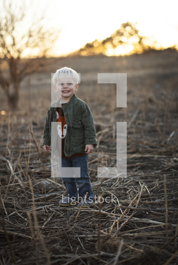 A toddler boy standing in a plowed field. 