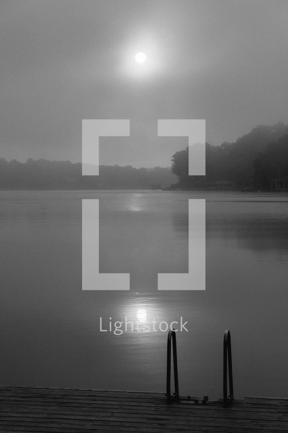 light of the full moon through the clouds over a lake and dock 