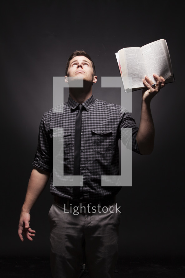 Man holding up Bible with one hand, looking to the heavens for answers,