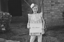 A little girl holding a He is Risen sign in black and white 