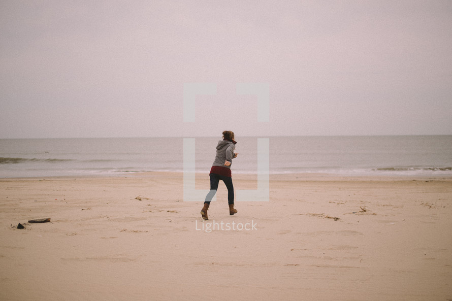 A woman on a beach jogs toward the ocean.
