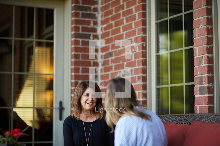 a mature woman and younger woman talking in conversation on a front porch