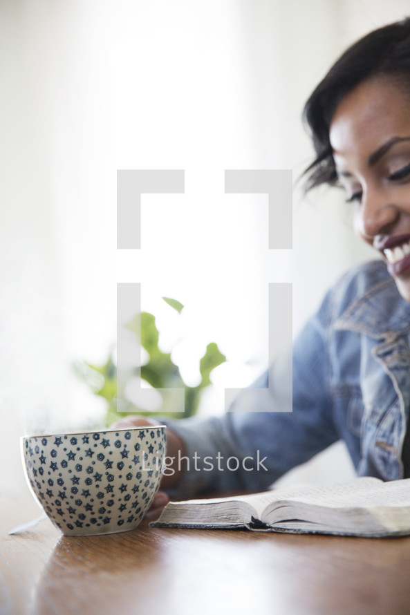 an African American woman sitting at a table reading a Bible 