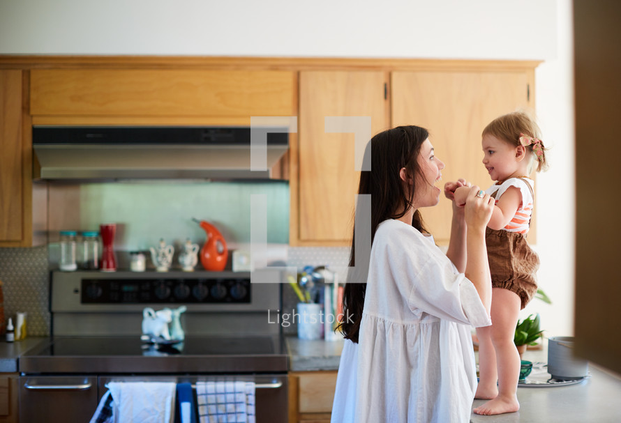 a mother talking to her toddler daughter who is standing on a countertop