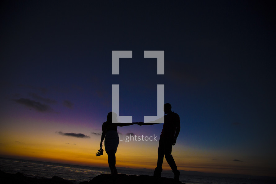 silhouette of a couple holding hands on a shore at sunset 