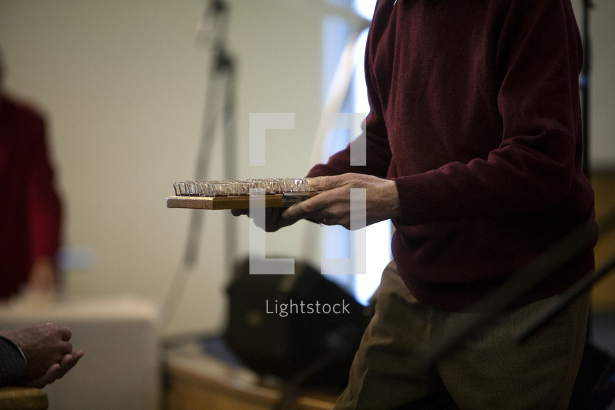 man carrying a tray of communion wine cups 