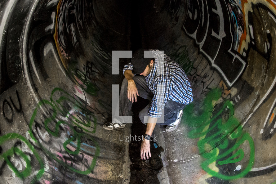 Man spray painting graffiti in a sewerdrain pipe.